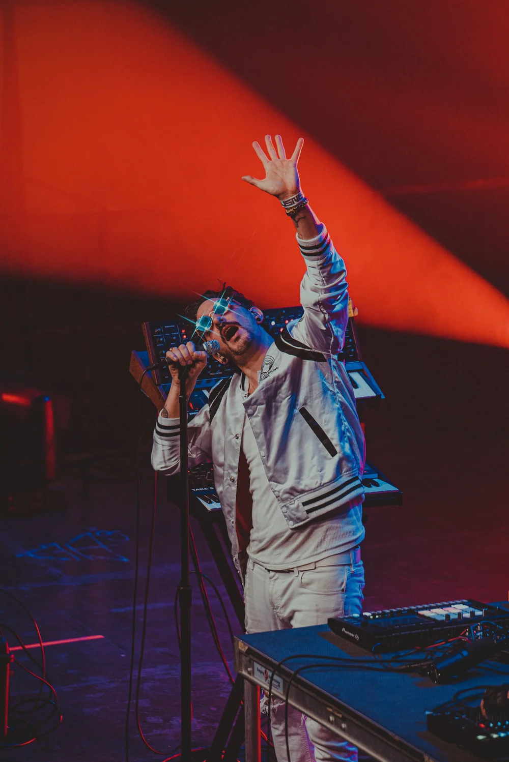 A performer raising a microphone beneath red stage lights