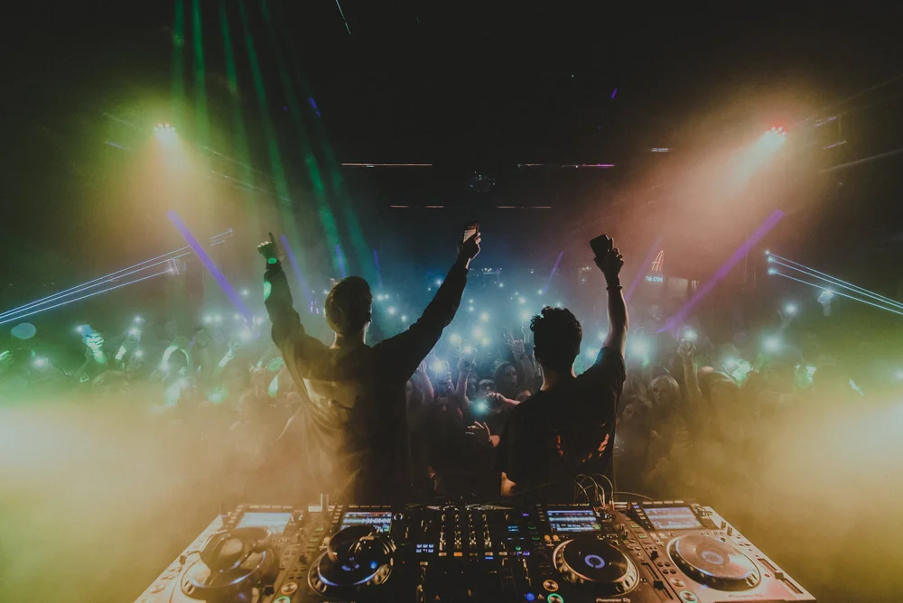 Two silhouettes raising their arms in front of a concert audience