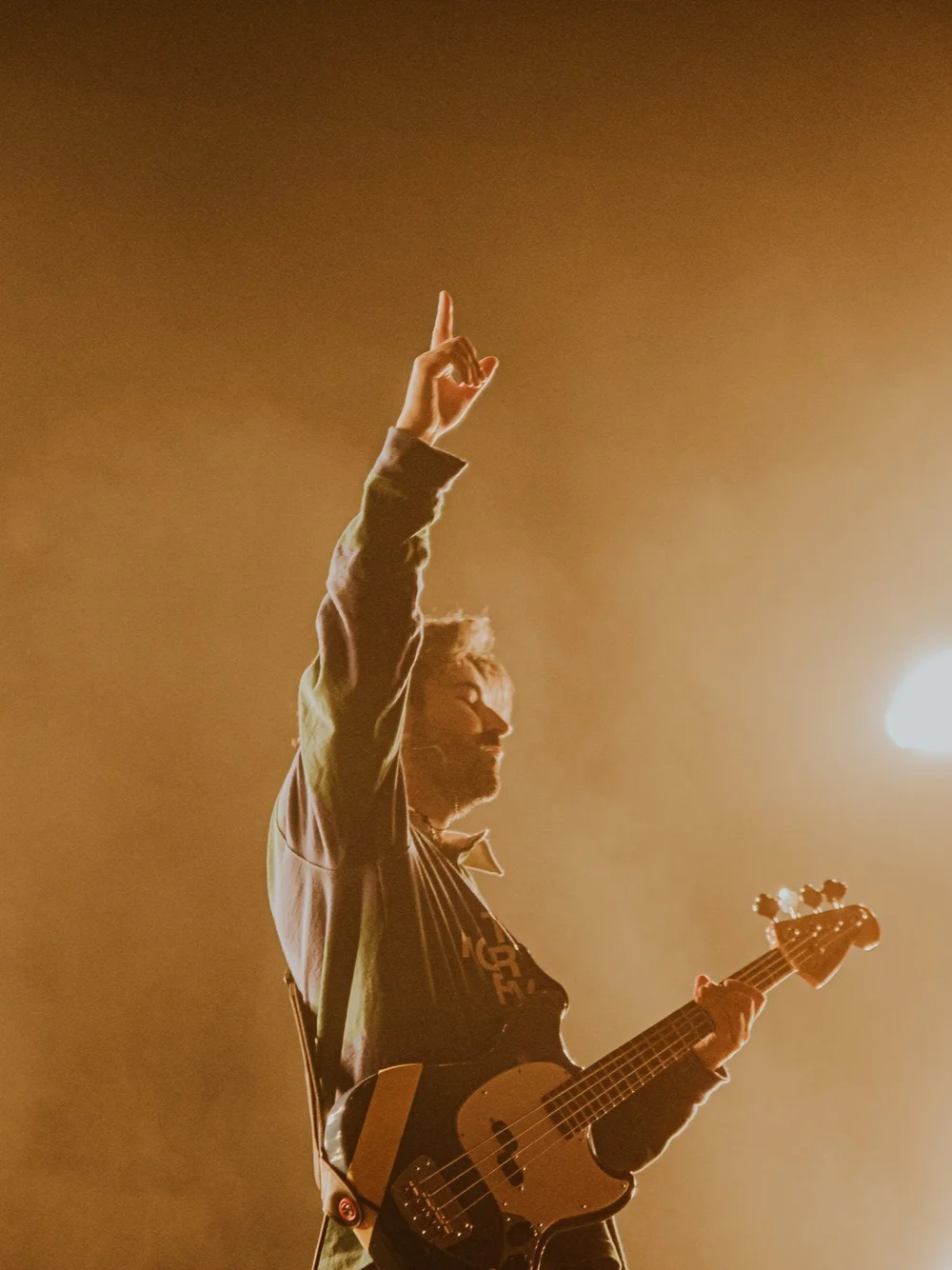 A guitarist raising one arm under warm stage lighting