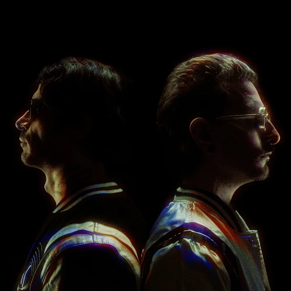 Two people standing back to back in coloured projected light