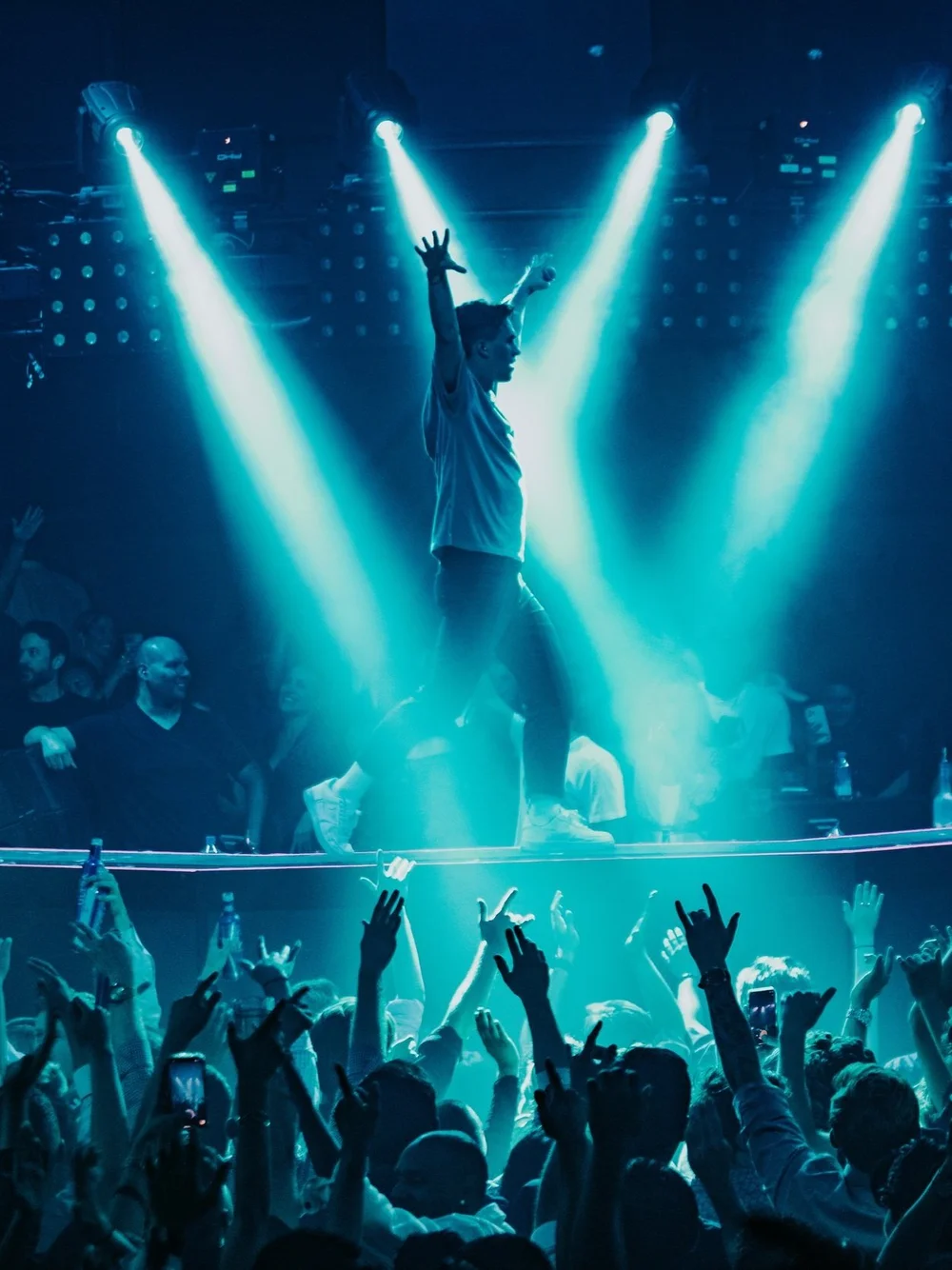 A concert audience beneath turquoise spotlights
